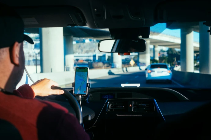 A person driving a car with a smartphone navigation app mounted on the dashboard